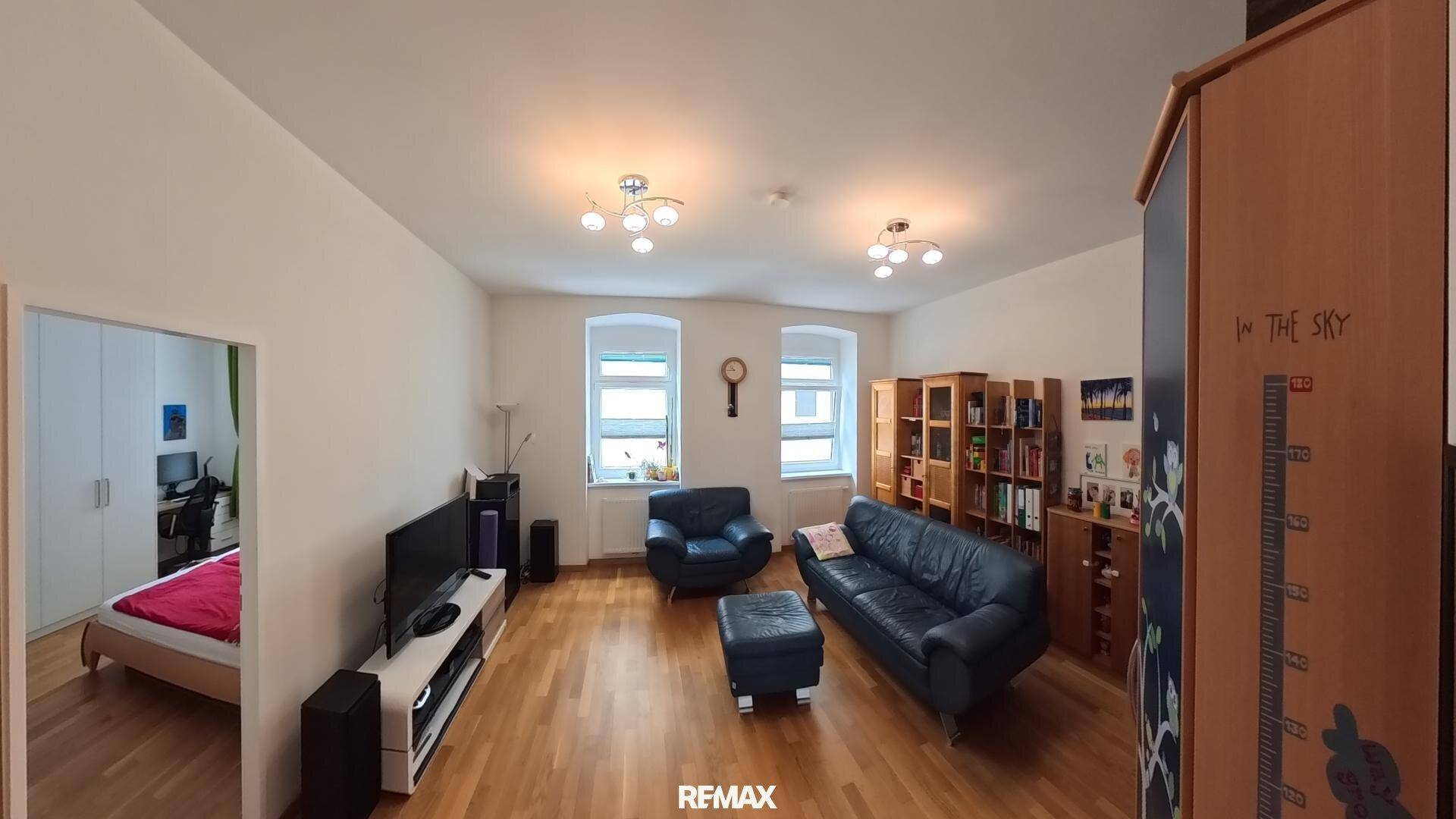 Gemütliches Wohnzimmer mit Holzboden, dunklen Sofas und Zugang zu einem angrenzenden Schlafzimmer.