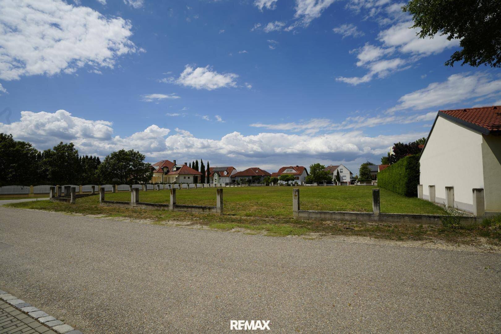 Weitwinkelansicht des grünen Grundstücks von der Straße, umgeben von Wohnhäusern und Bäumen.