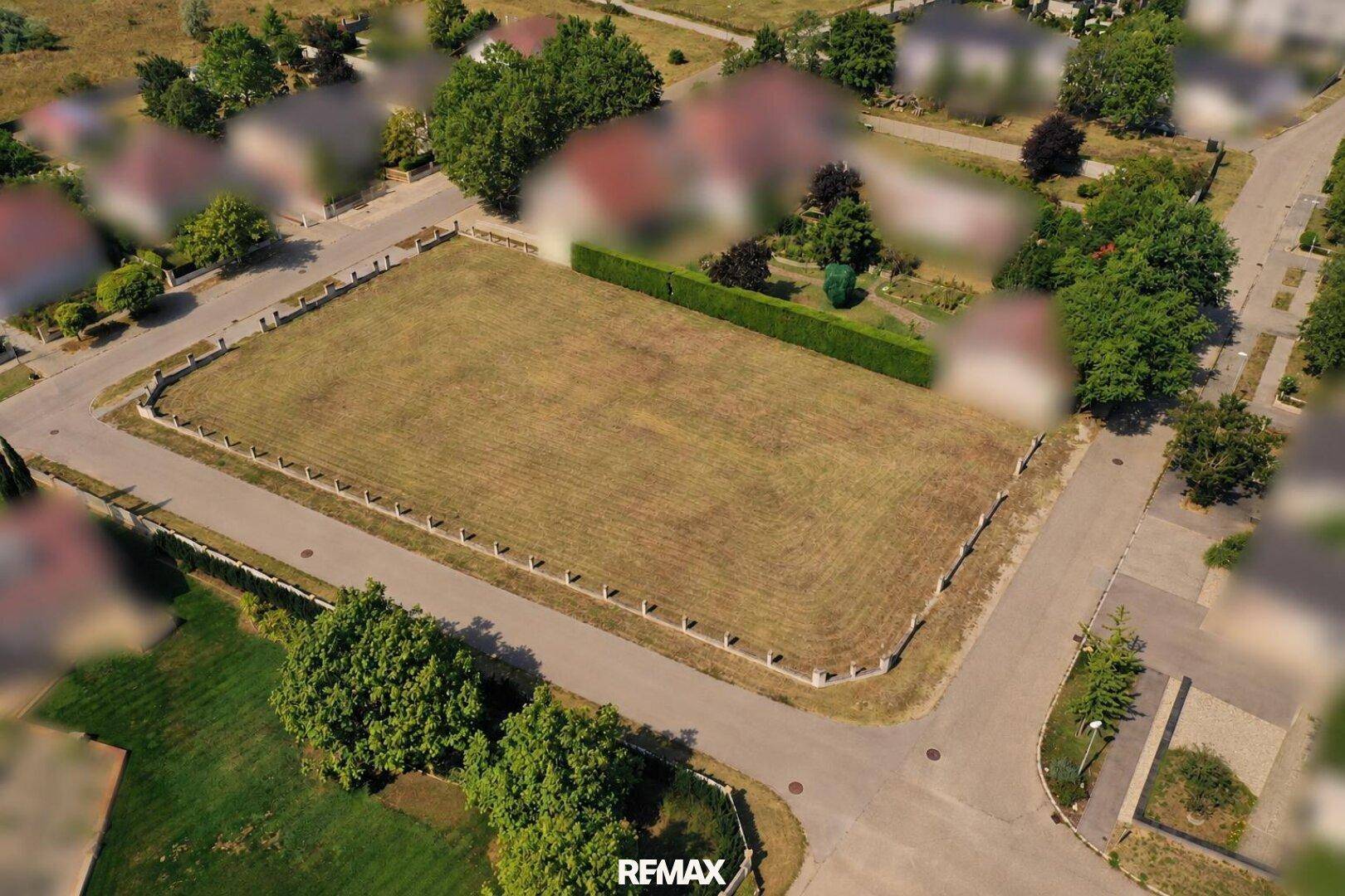 Luftaufnahme des Grundstücks mit trockener Rasenfläche, umgeben von Wohngebäuden und Straßen.