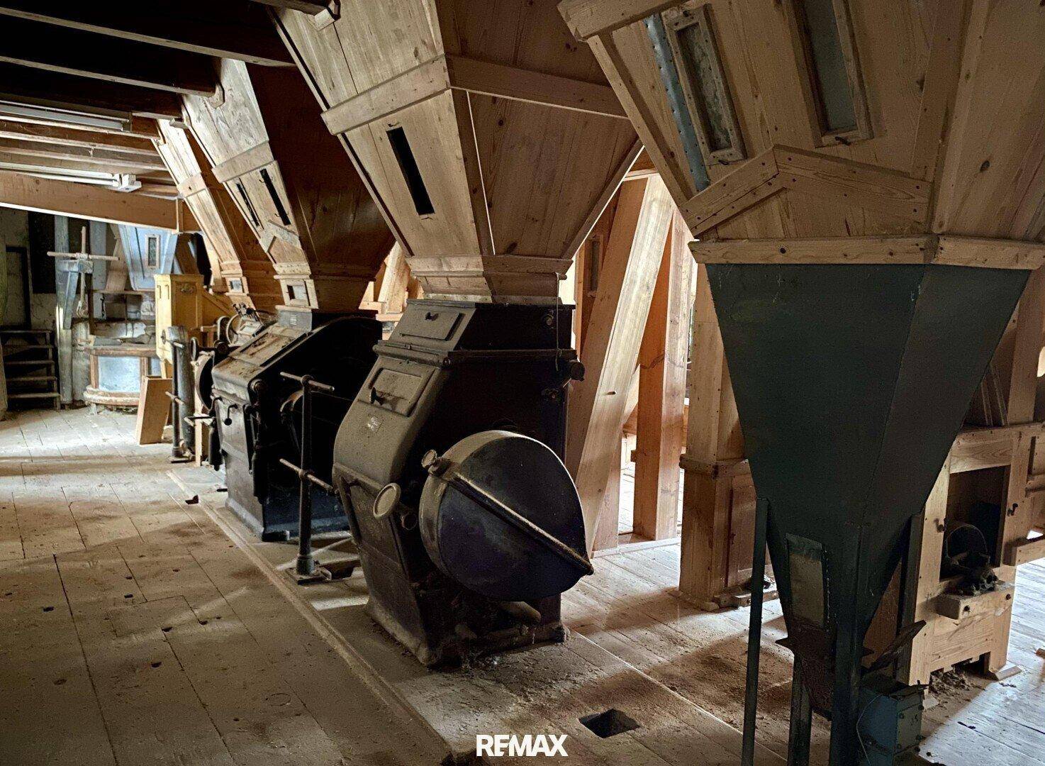 Historische Mühlenmaschinen aus Holz und Metall in einem großen Innenraum mit Holzboden.