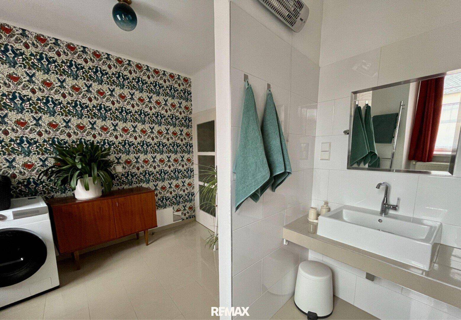 Modernes Badezimmer mit weiß gefliesten Wänden, Waschbecken und einem Bereich mit floraler Tapete.