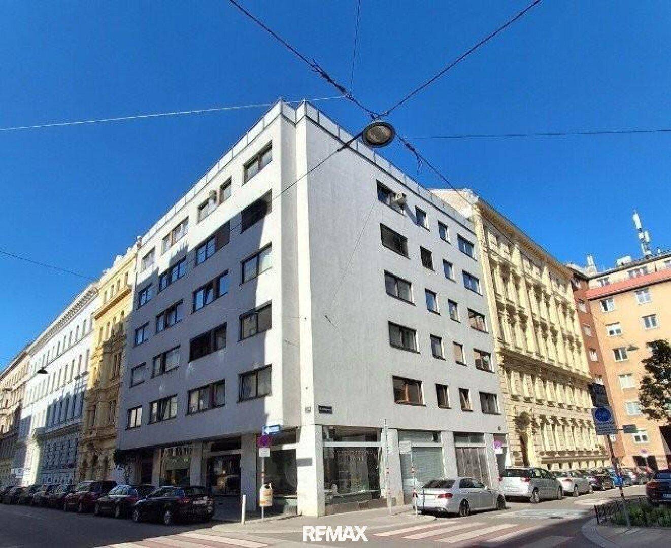 Modernes Eckgebäude in der Stadt mit vielen Fenstern und parkenden Autos.