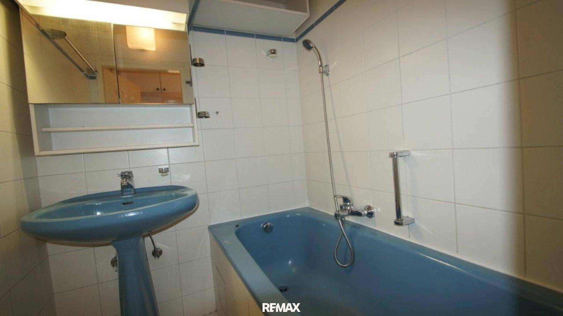 Badezimmer mit blauer Badewanne, Waschbecken und weißen Fliesen.