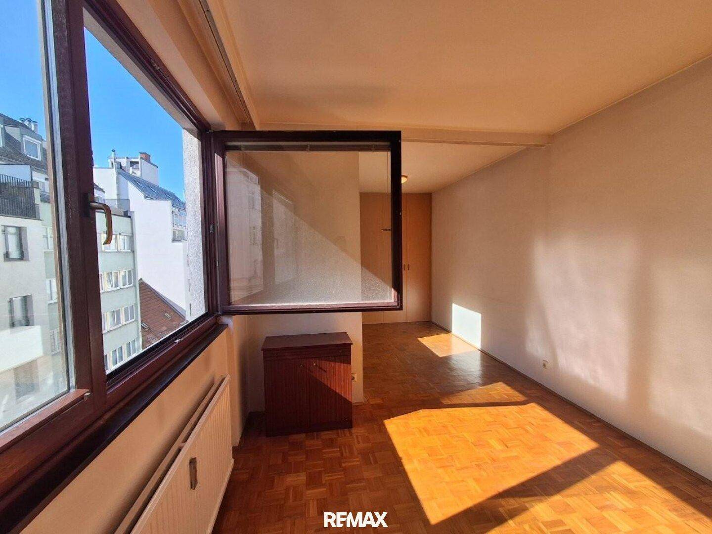 Schlafzimmer mit Parkettboden, Einbauschränken und Blick auf die umliegenden Gebäude.