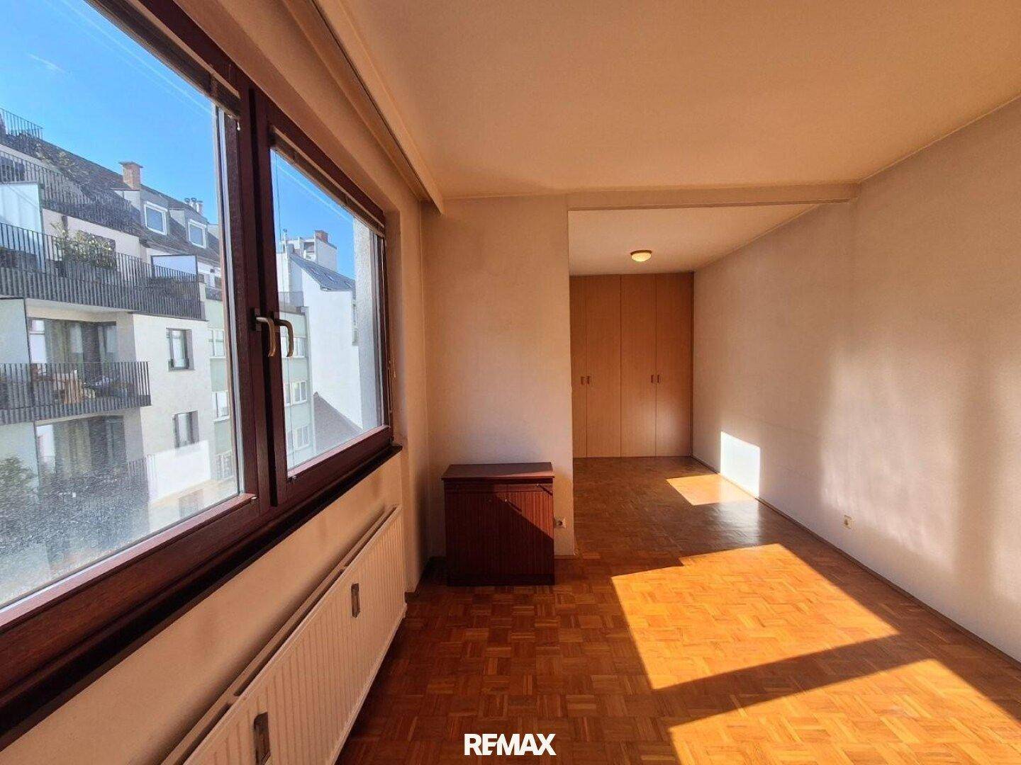 Schlafzimmer mit Parkettboden, Einbauschränken und Blick auf die umliegenden Gebäude.