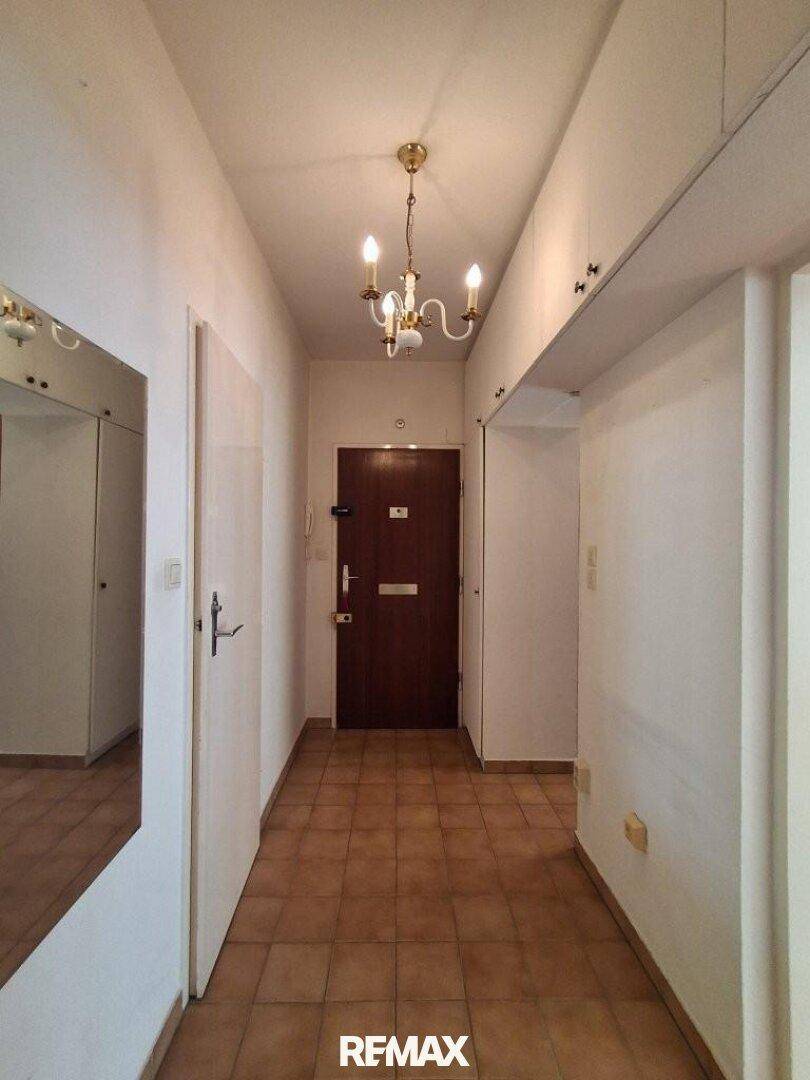 Heller Flur mit Fliesenboden, Spiegelschrank und dunkler Eingangstür.