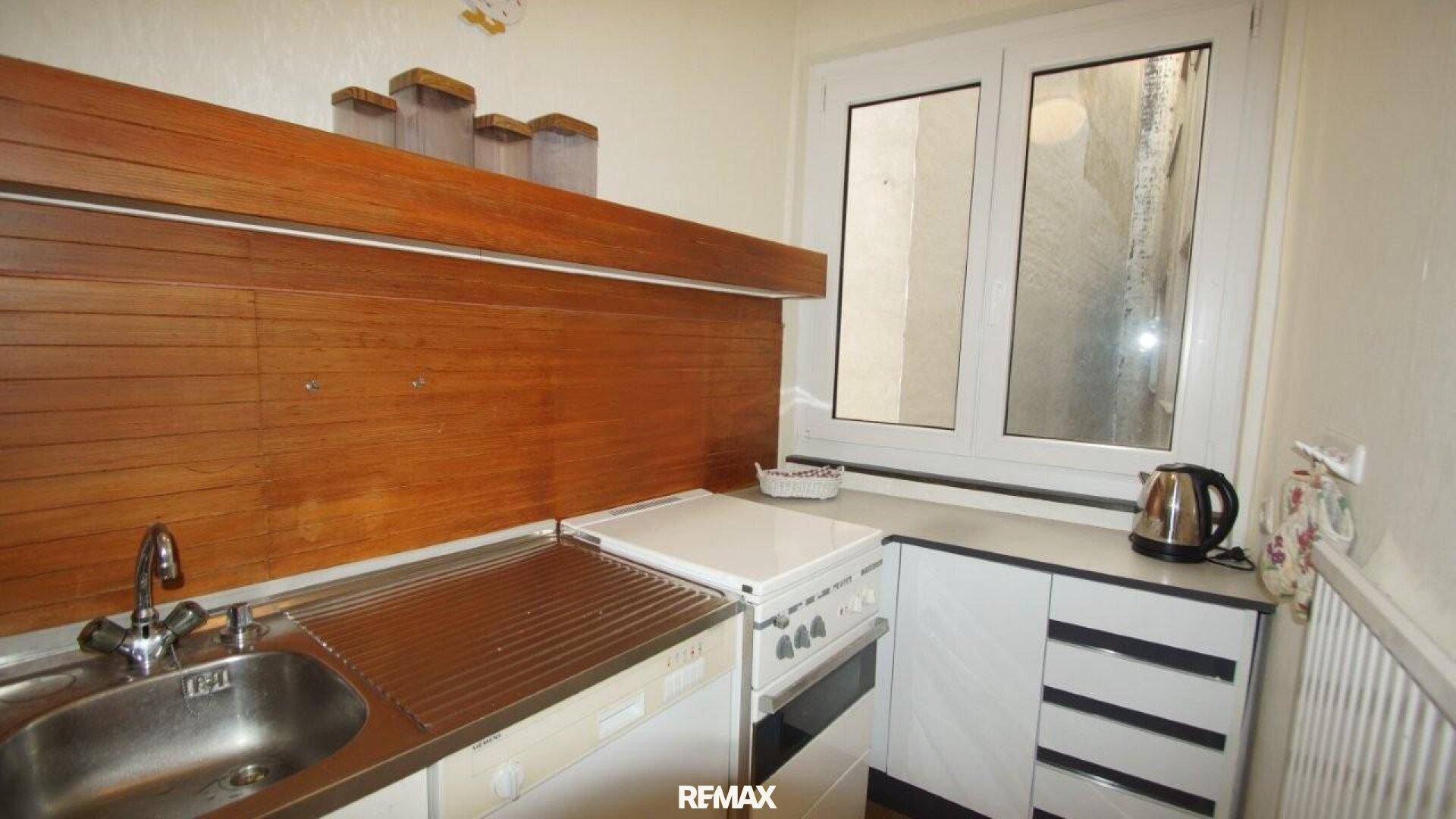 Kleine Küche mit weißer Einbauküche, Holzrückwand und Fenster.