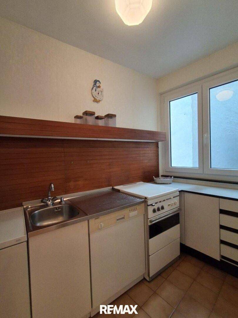 Kleine Küche mit weißer Einbauküche, Holzrückwand und Fenster.