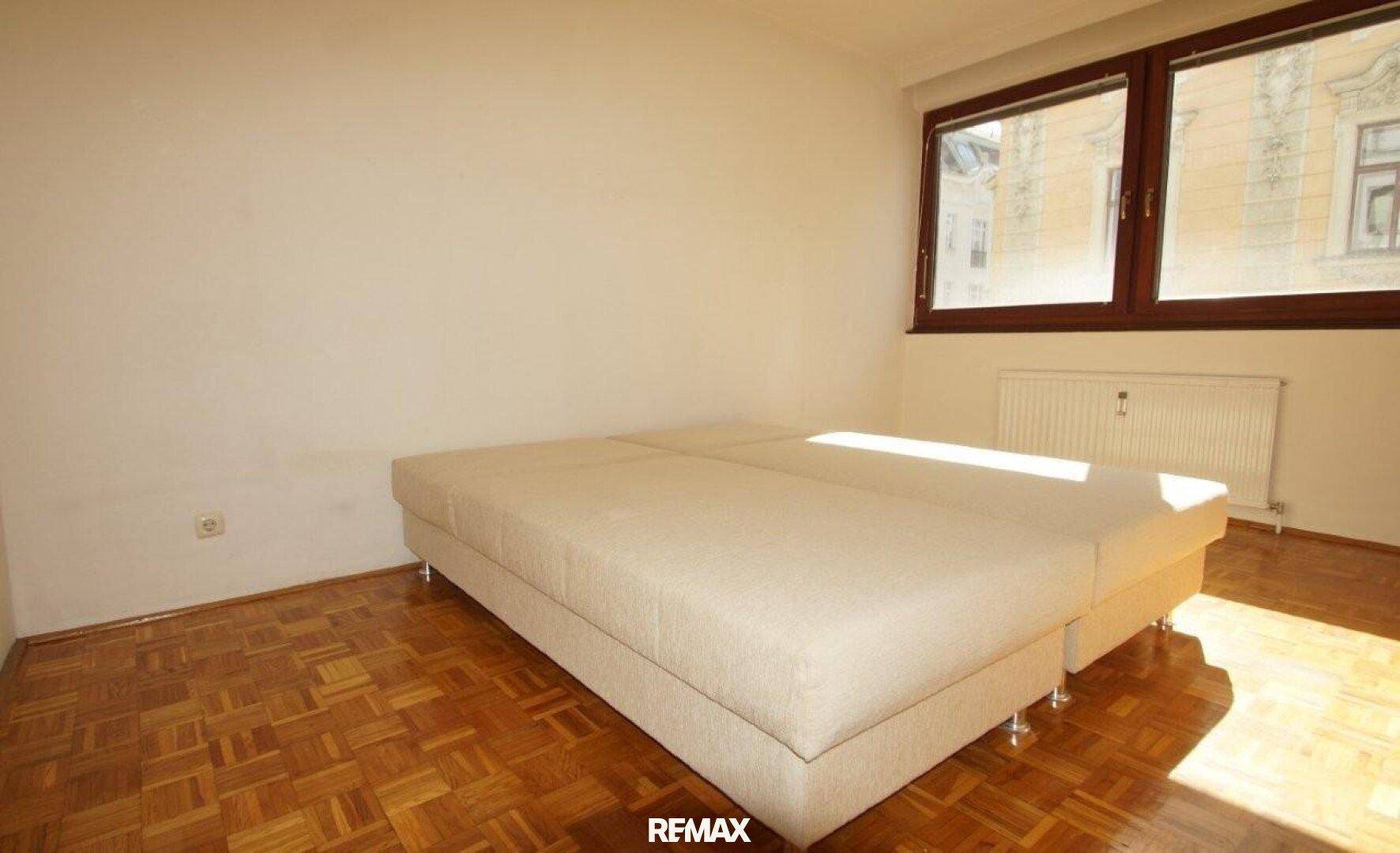 Schlafzimmer mit Parkettboden und einem großen, hellen Bettgestell.