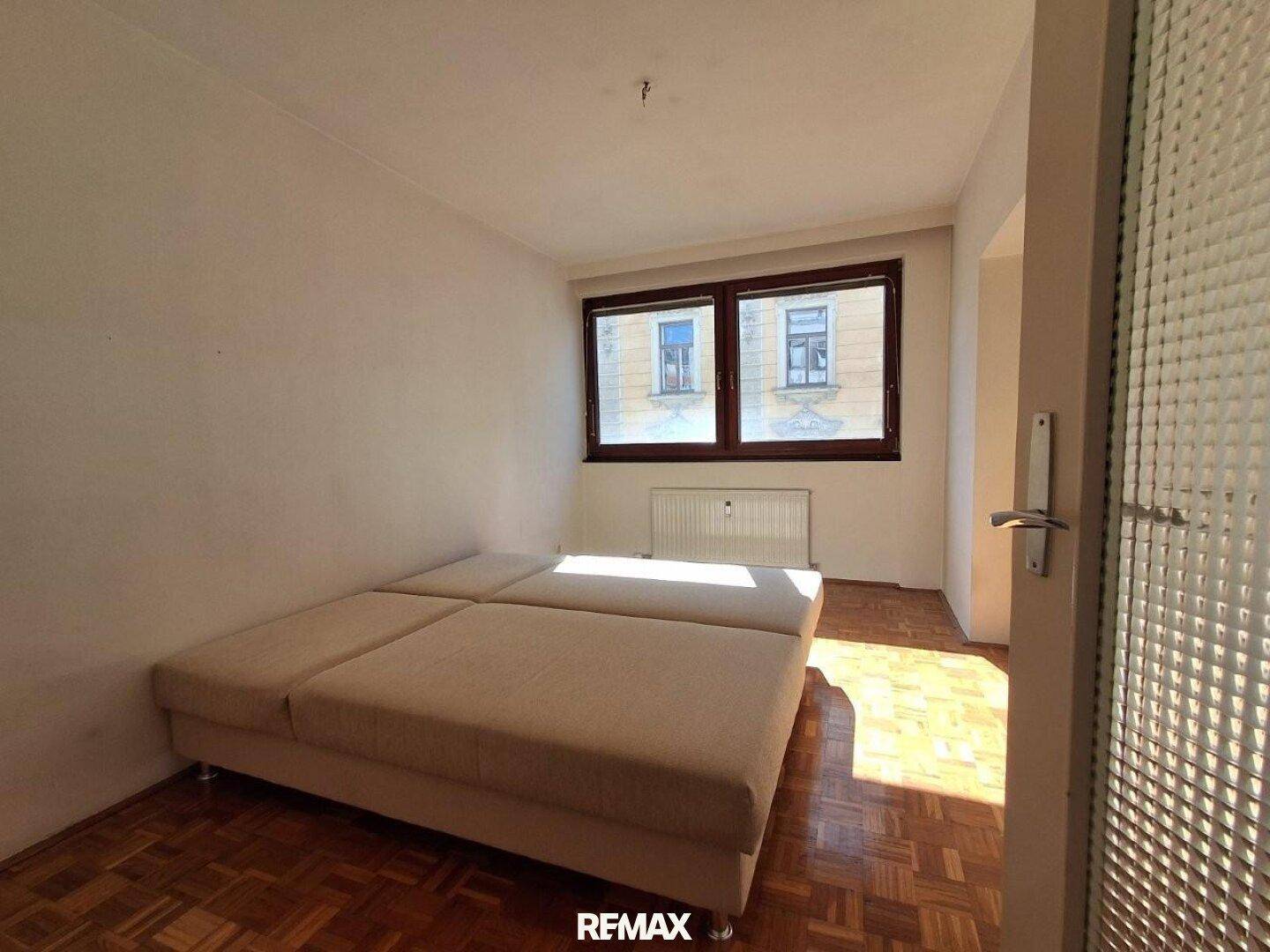 Schlafzimmer mit Parkettboden und einem großen, hellen Bettgestell.