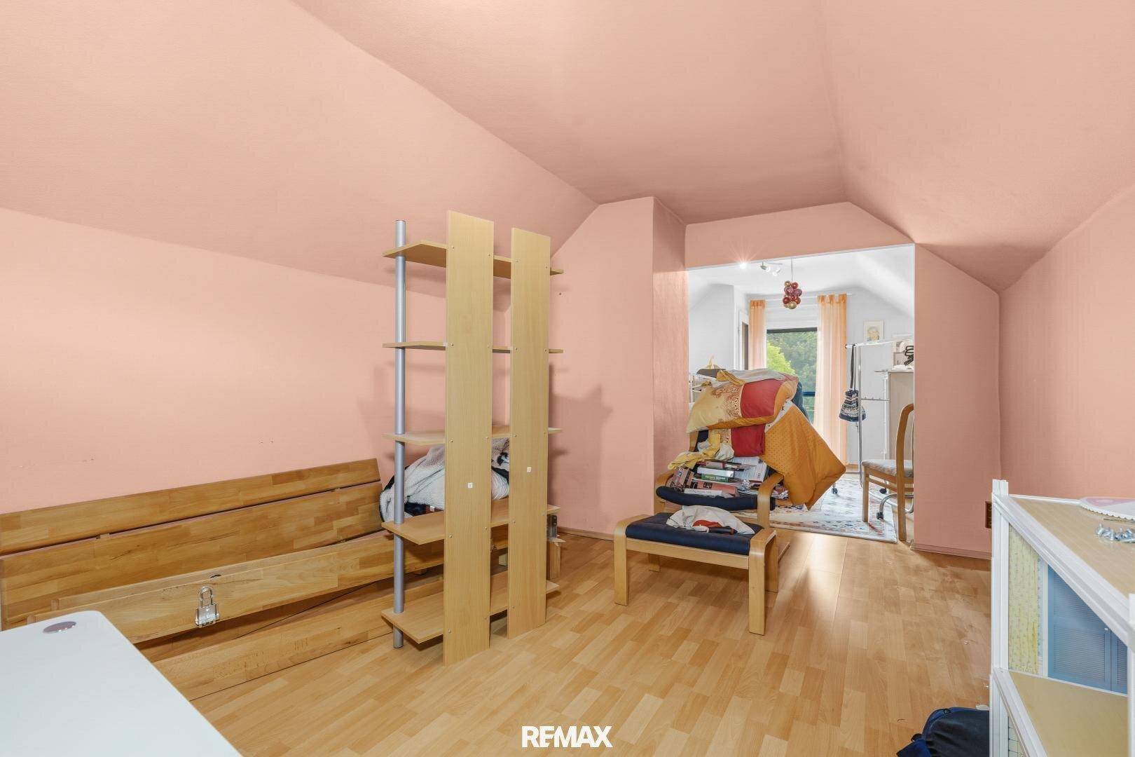 Dachzimmer mit schrägen Wänden, rosa Anstrich und Parkettboden, offen zu einem angrenzenden Bereich.