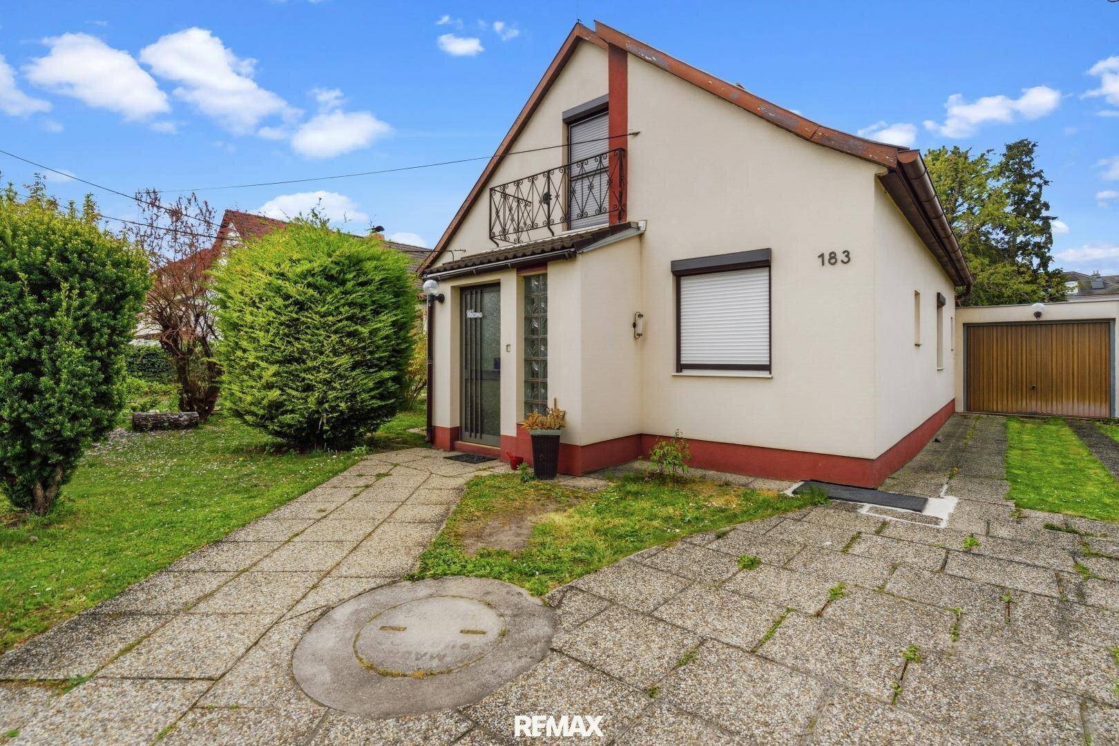 Vorderansicht des Hauses mit Vorgarten, Einfahrt und einem französischen Balkon im Obergeschoss.