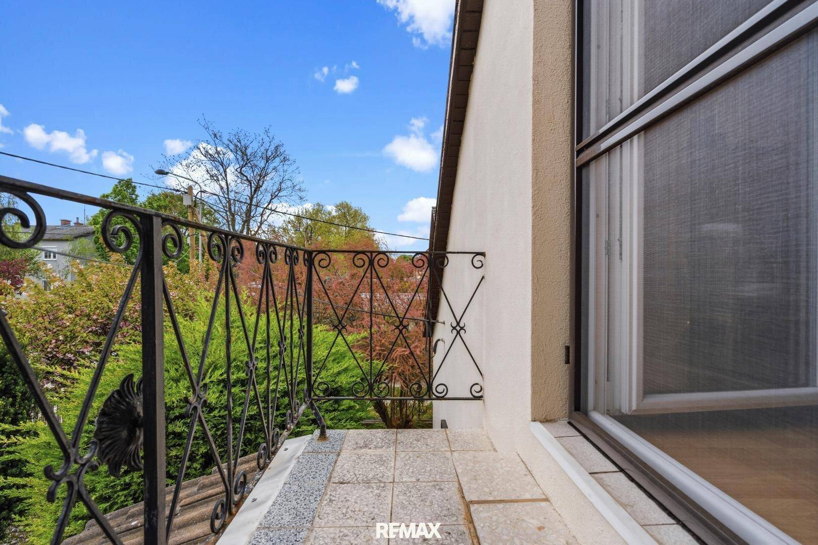 Kleiner Balkon mit schmiedeeisernem Geländer und Fliesenboden, mit Blick ins Grüne.