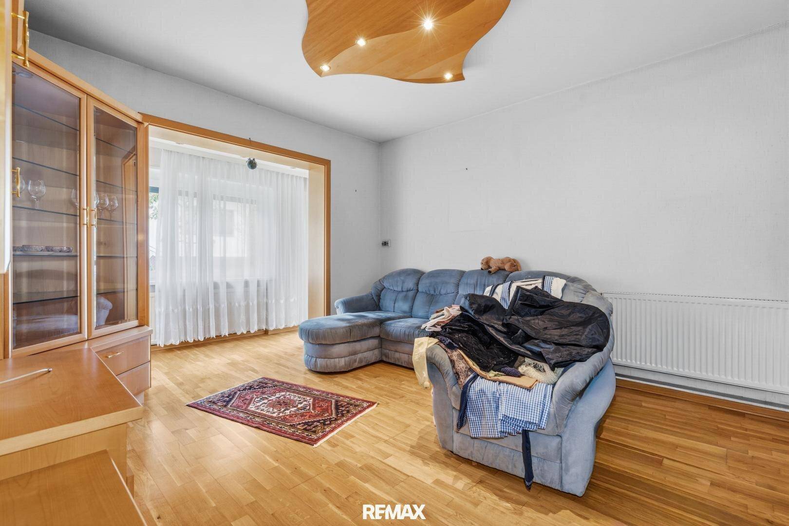 Helles Wohnzimmer mit blauem Sofa, Holzmöbeln und Parkettboden, mit Blick auf den Garten.