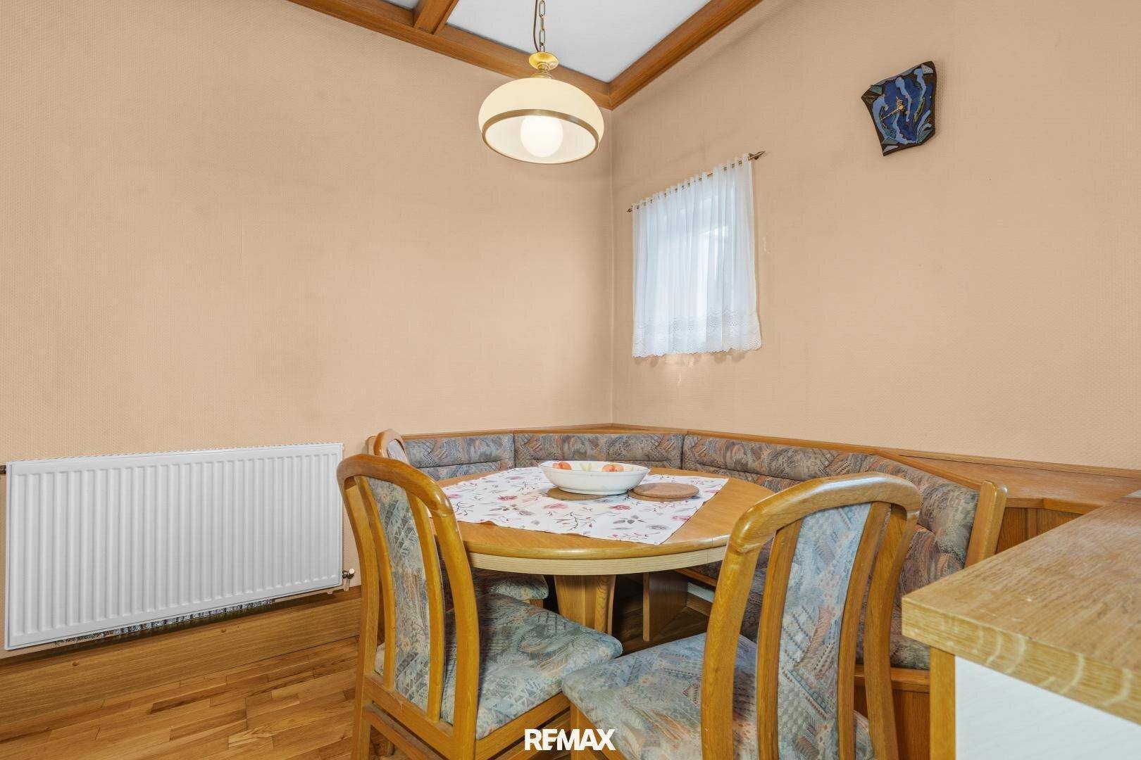 Essbereich in der Küche mit traditioneller Eckbank, Holztisch und einem Heizkörper unter dem Fenster.