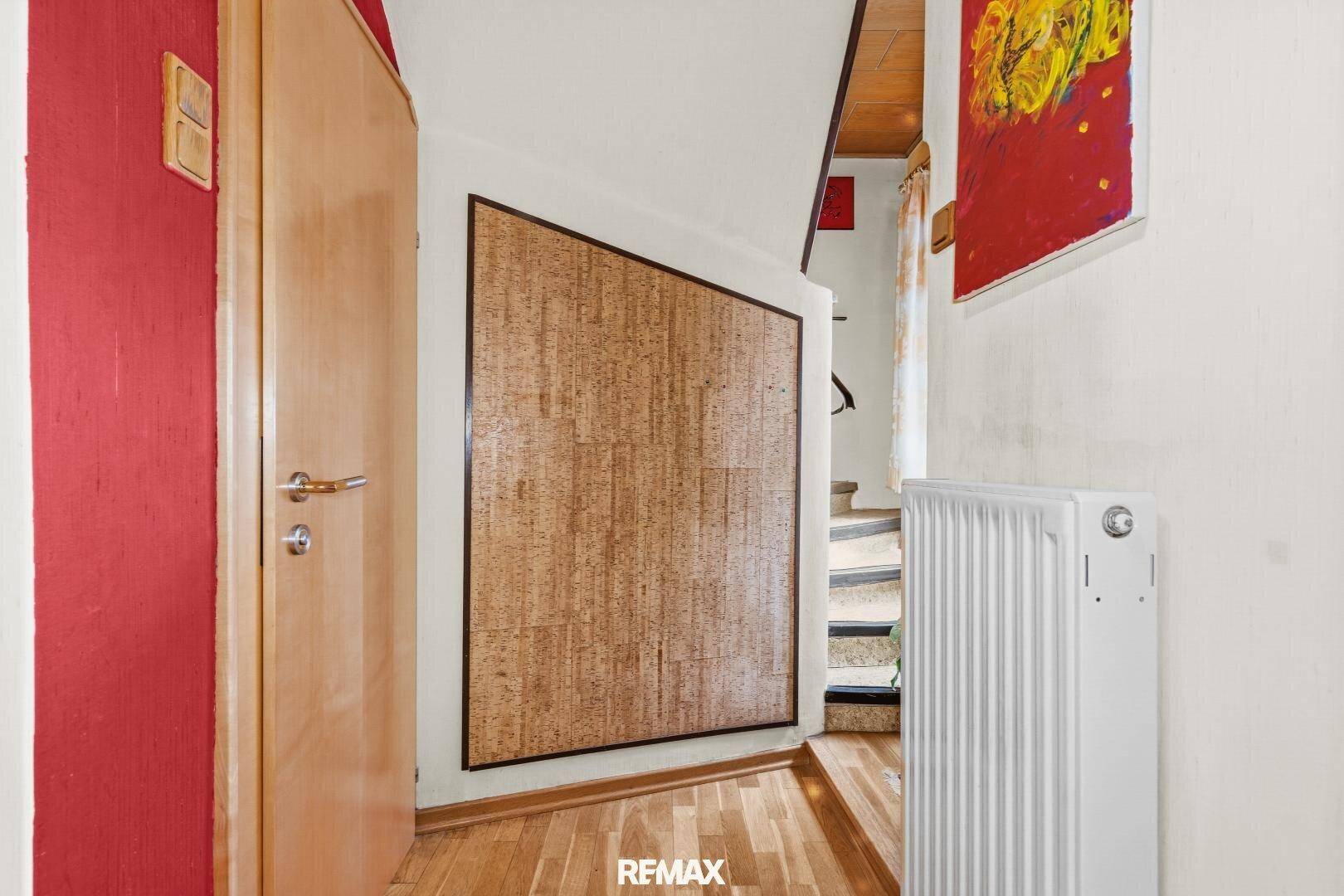 Flur- und Treppenhausbereich mit Heizkörper, Holztür und einer strukturierten Wandverkleidung.