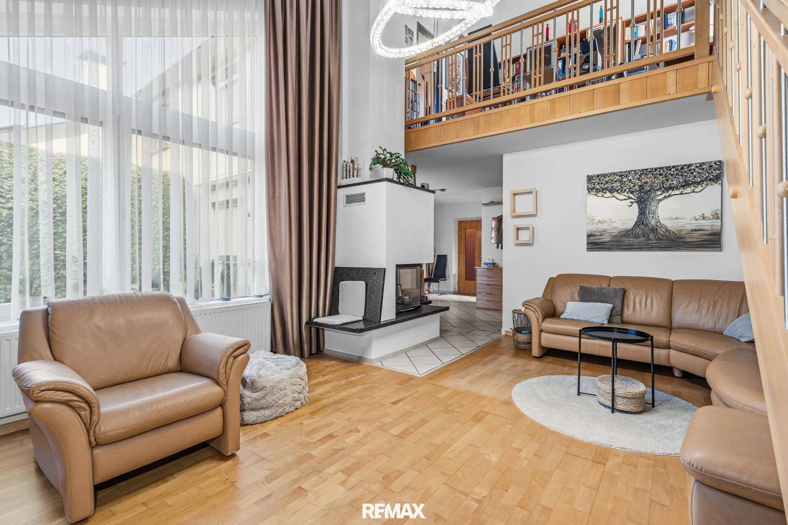 Helles Wohnzimmer mit hohen Decken, Kamin und Galeriebereich mit Holzgeländer.