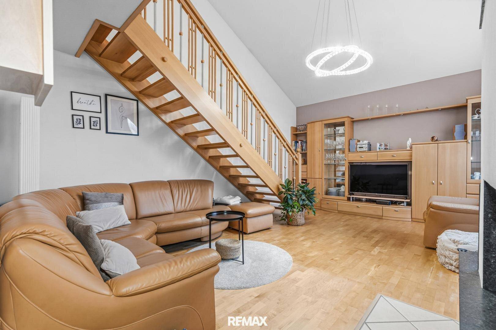 Gemütliches Wohnzimmer mit Ledersofa, Holztreppe zur Galerie und integriertem Mediensystem.