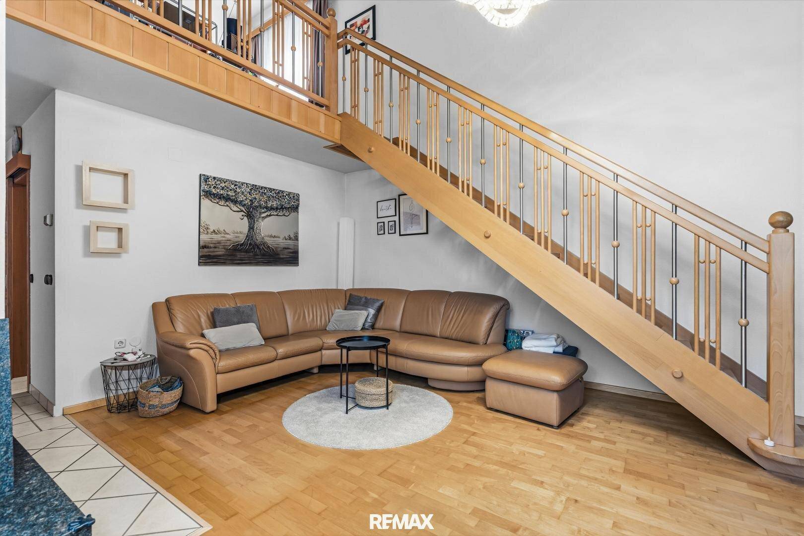 Gemütliches Wohnzimmer mit Ledersofa, Holztreppe und hellem Parkettboden.