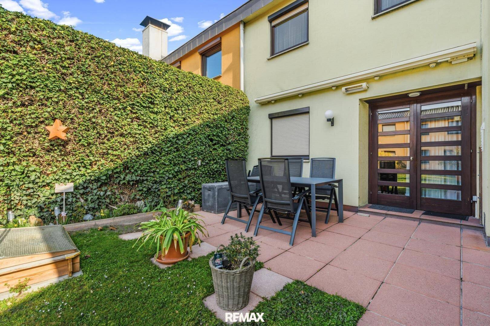 Gemütliche Terrasse mit Sitzgelegenheiten und einer grünen Hecke als Sichtschutz.