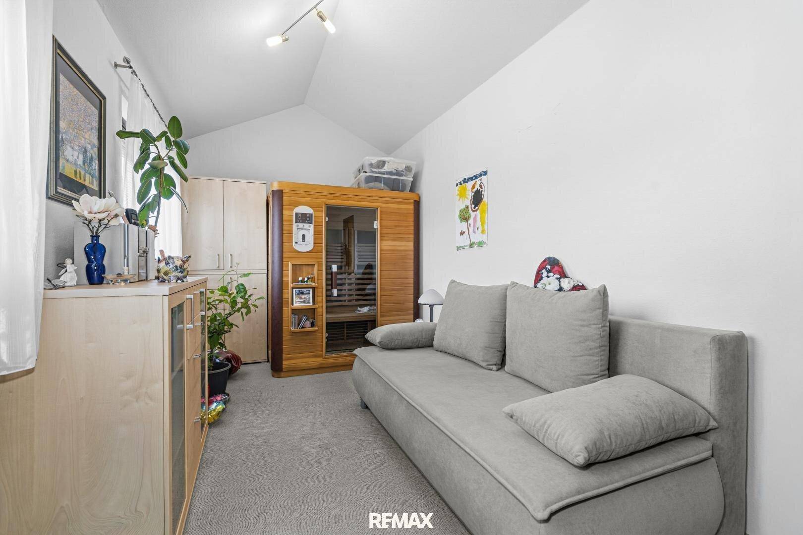 Raum mit Sofa, Teppichboden und einer sichtbaren Sauna-Kabine.