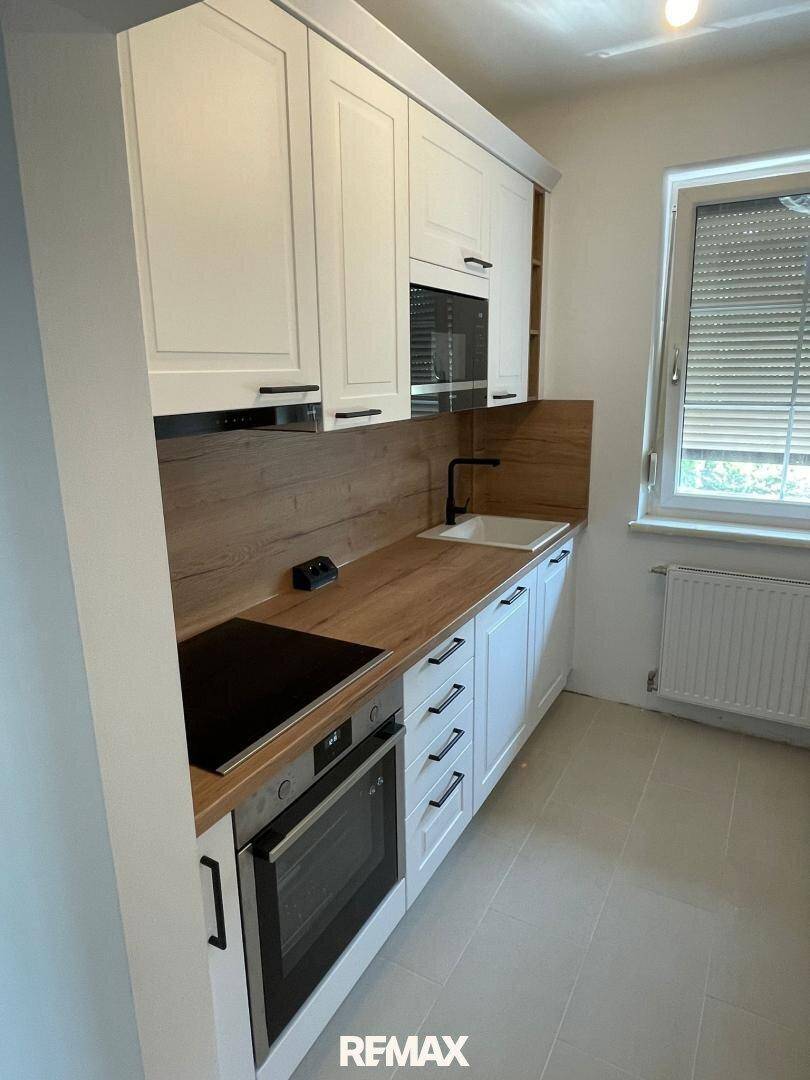 Helle, moderne Küche mit weißen Schränken, Holzarbeitsplatte und Fenster.