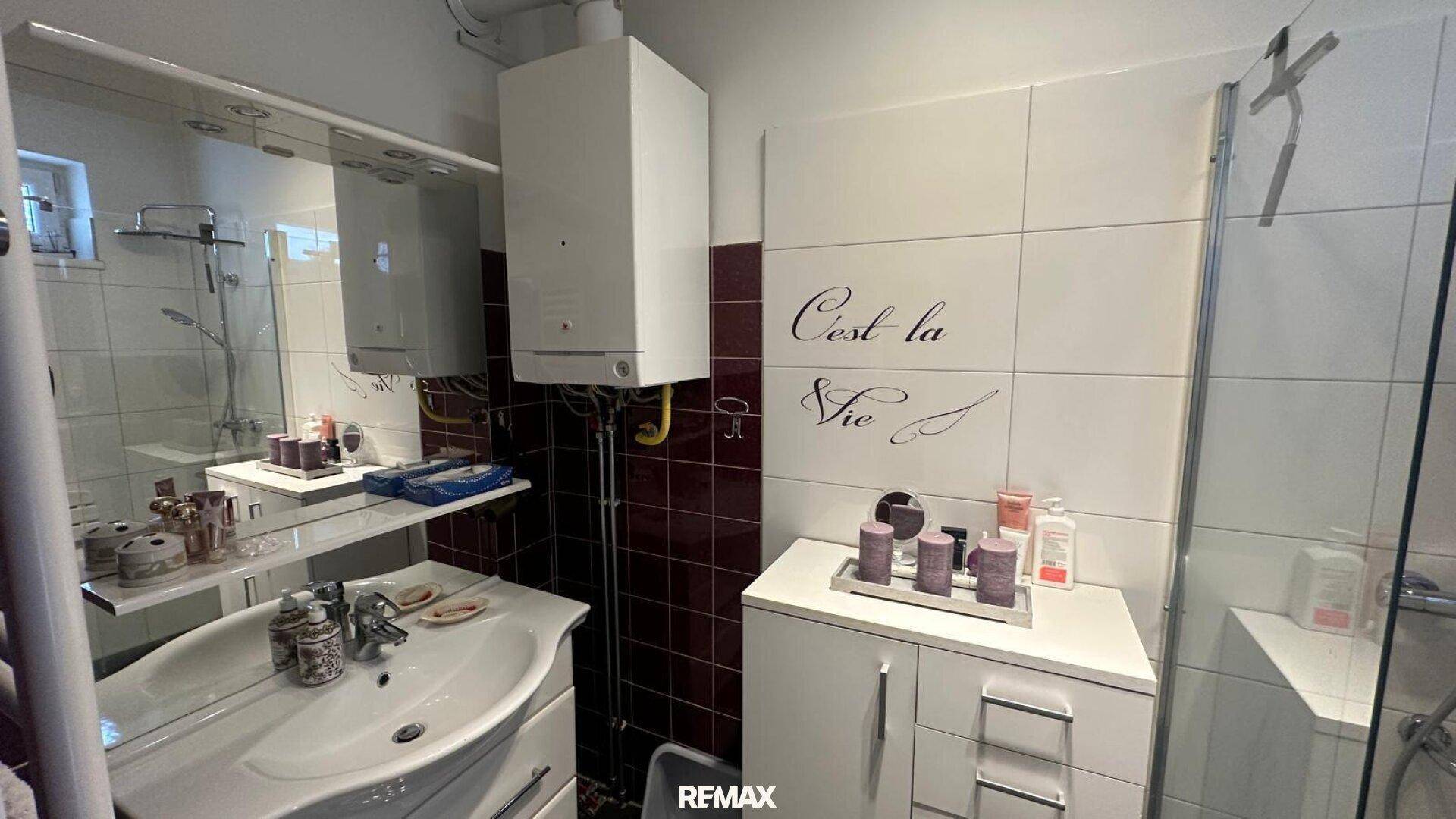 Badezimmer mit Dusche, Waschbecken und Gastherme, teilweise gefliest.