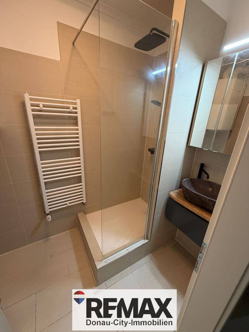 Modernes Badezimmer mit ebenerdiger Dusche, Handtuchheizkörper und stilvollem Waschbecken.