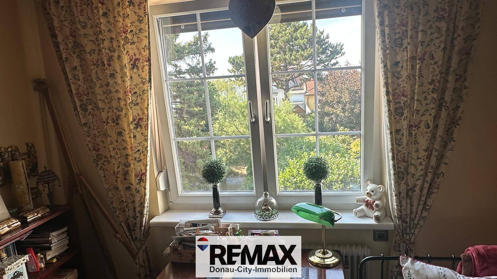 Fenster mit Vorhängen und Blick auf grüne Bäume und die Umgebung.