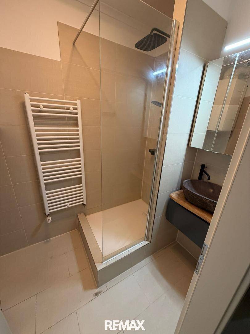 Modernes Badezimmer mit ebenerdiger Dusche, Handtuchheizkörper und dunklem Waschbecken.