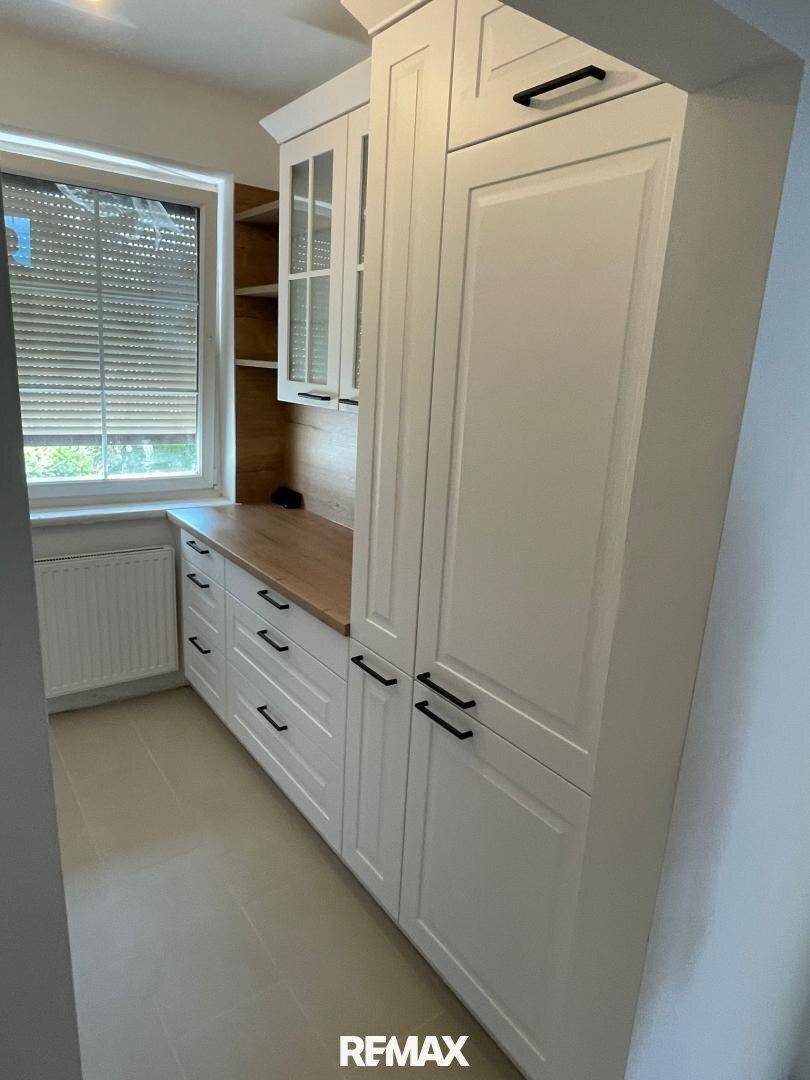 Hohe Küchenschränke mit weißen Fronten und Holzdetails, bieten viel Stauraum.