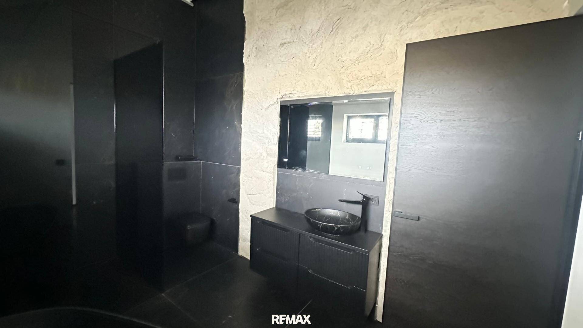 Elegantes Badezimmer mit dunklen Fliesen, modernem Waschbecken und Spiegel, in luxuriösem Stil.