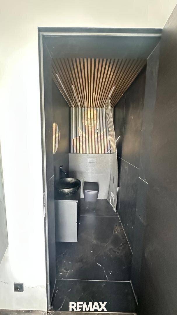 Modernes Gäste-WC mit dunklen Fliesen, stilvollem Waschbecken und Holzlamellen an der Decke.