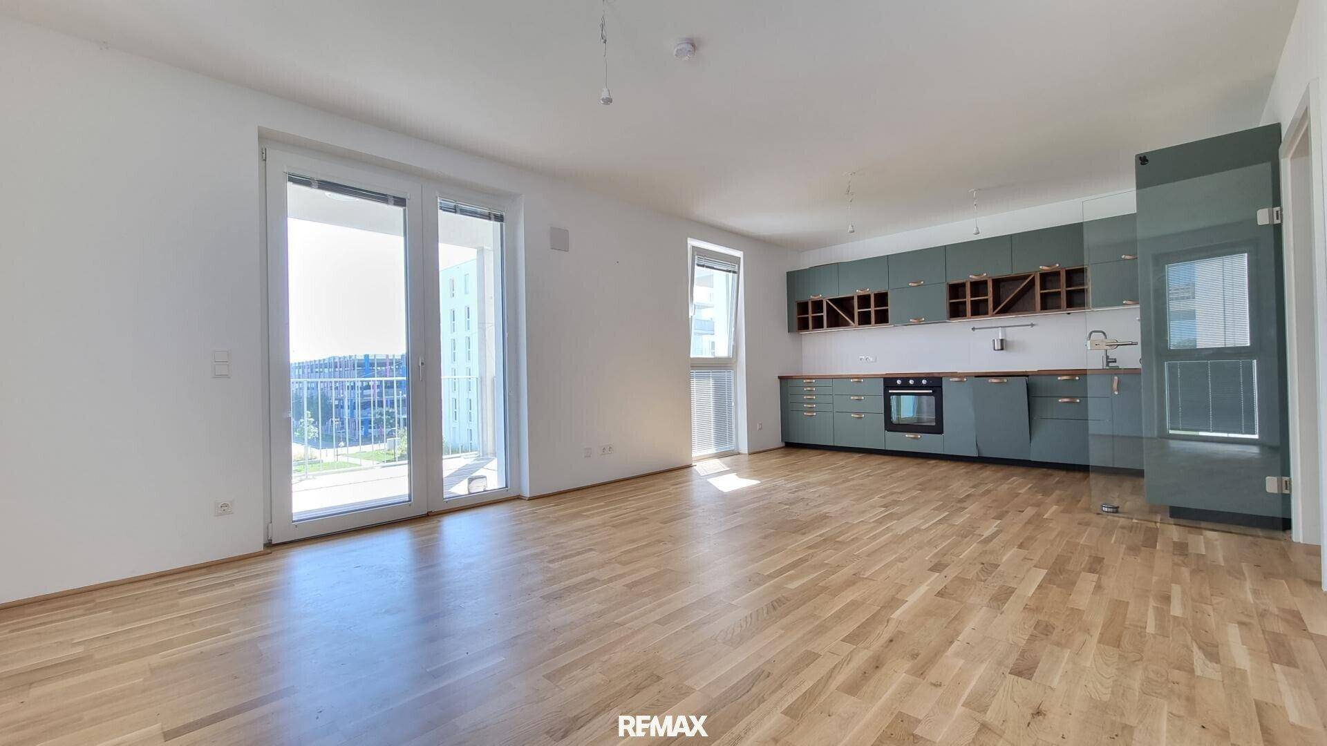 Heller offener Wohnbereich mit integrierter Küche und Zugang zu einem Balkon, bietet viel Tageslicht.