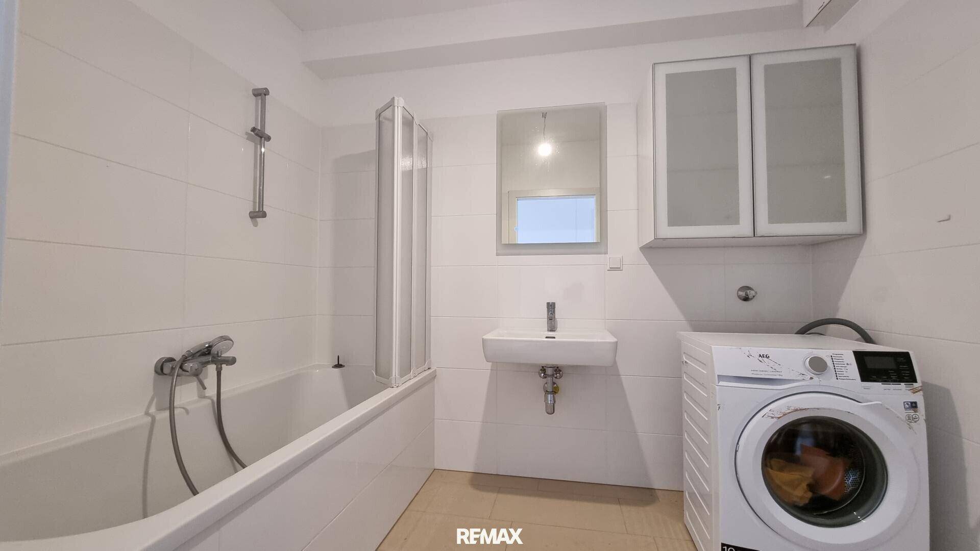 Funktionales Badezimmer mit Badewanne, Waschbecken und Waschmaschine, hell gefliest für einfache Pflege.