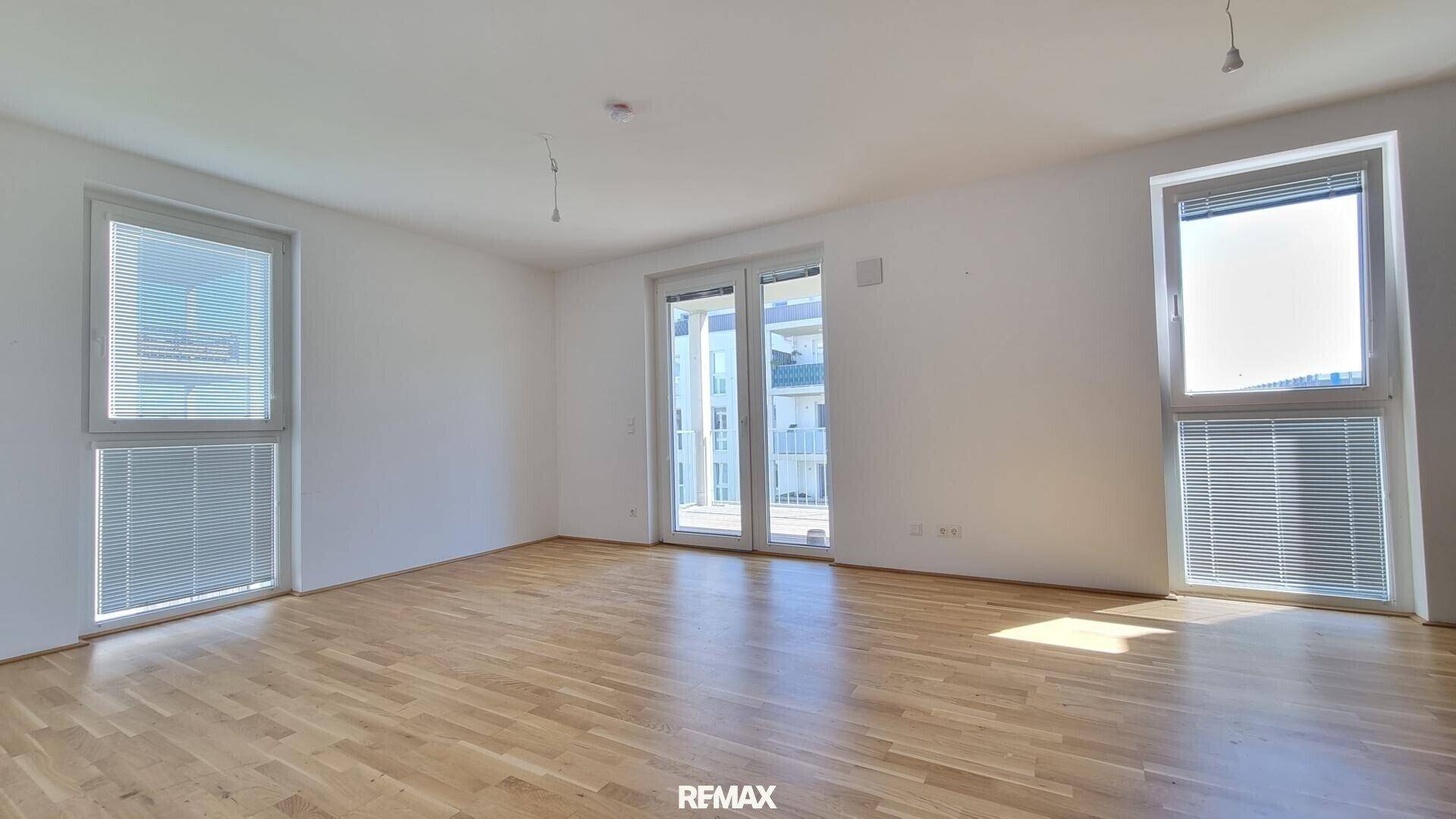 Geräumiger, heller Raum mit Holzboden und großen Fenstern, die viel natürliches Licht hereinlassen.
