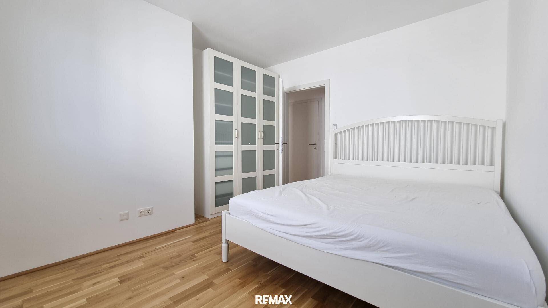 Helles Schlafzimmer mit weißem Bett und Kleiderschrank, ausgestattet mit Holzboden für gemütliches Wohnen.