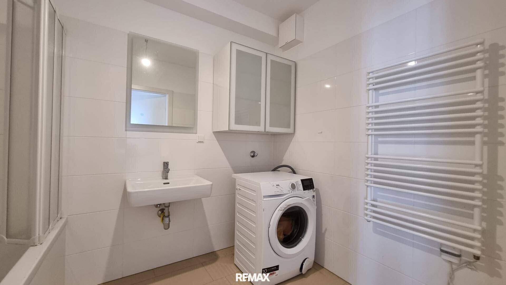 Modernes Badezimmer mit Waschbecken, Waschmaschine und beheiztem Handtuchhalter, komplett gefliest.