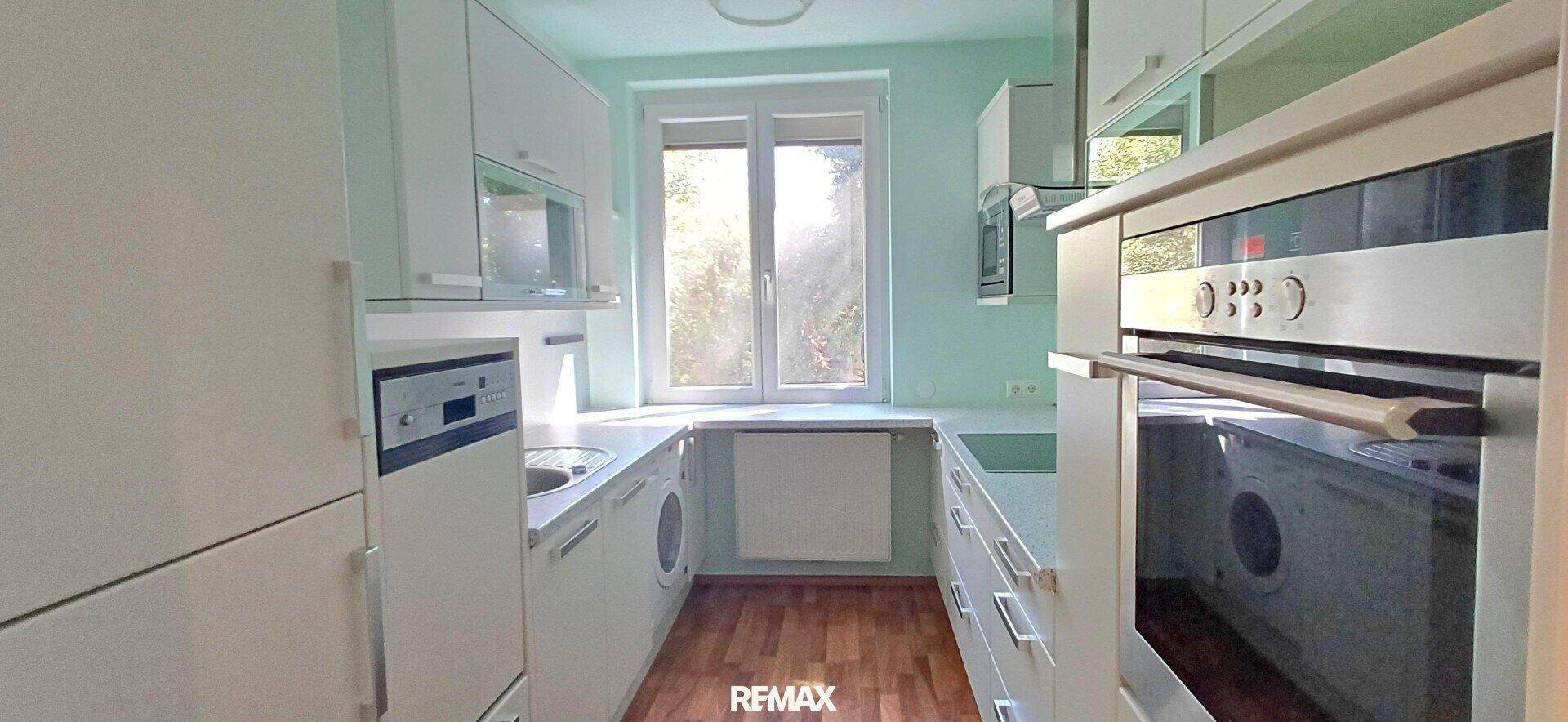 Moderne Küche mit weißen Schränken, integrierten Geräten und einem Fenster mit Blick ins Grüne.