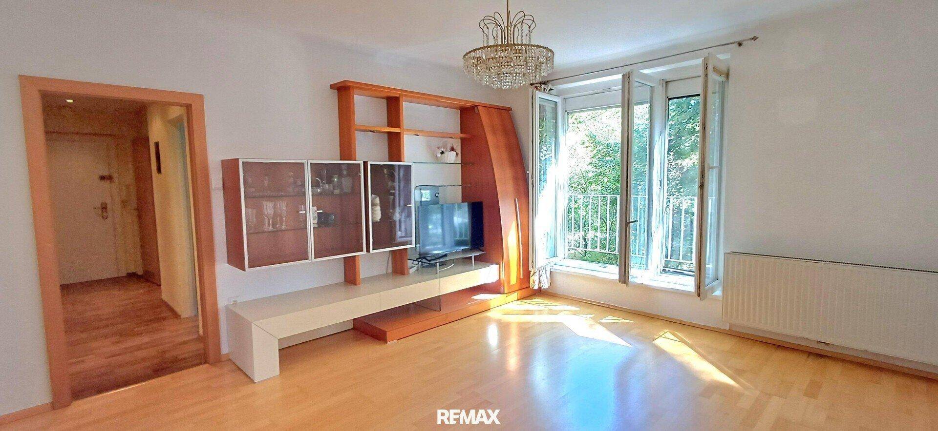 Helles Wohnzimmer mit Parkettboden, großen Fenstern und einem eleganten Kronleuchter.