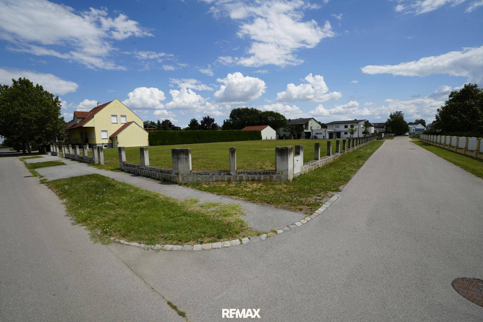 Eckansicht eines unbebauten Grundstücks mit niedriger Betonmauer und umliegenden Straßen.