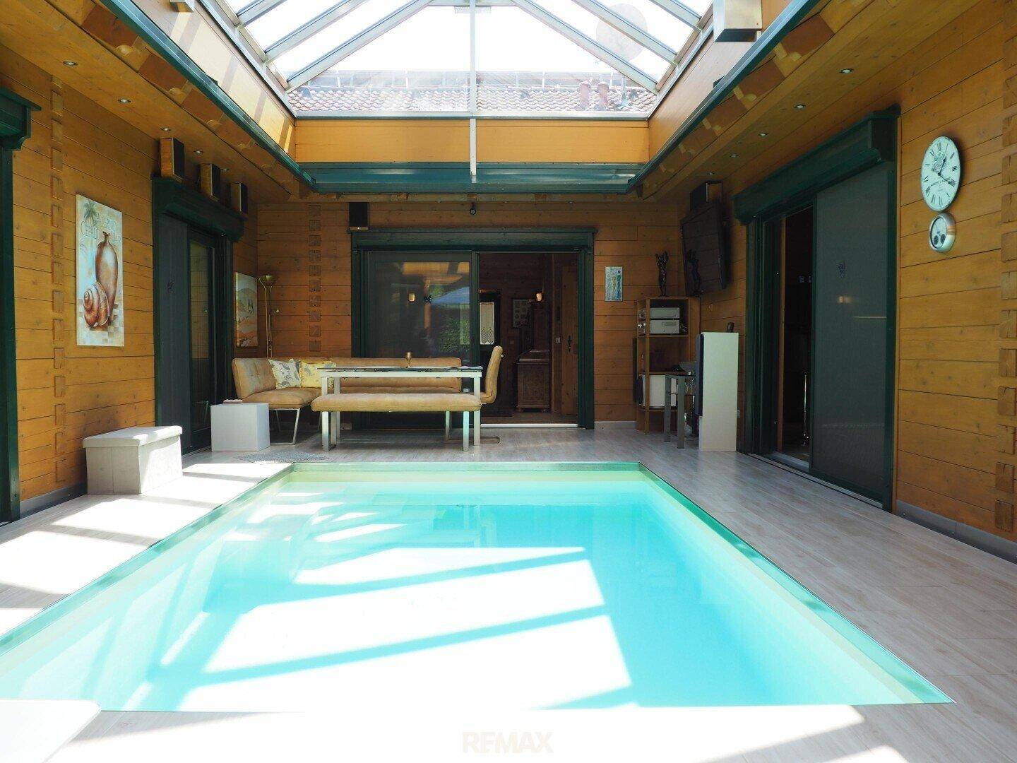 Geräumiger Wintergarten mit Pool und Essbereich, umgeben von warmen Holzverkleidungen.