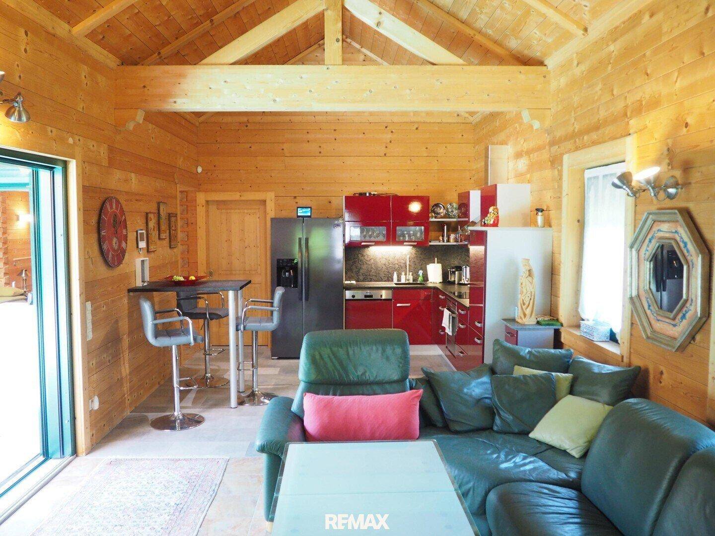 Offener Wohnbereich mit roter Küche, Ledersofa und sichtbaren Holzdeckenbalken.