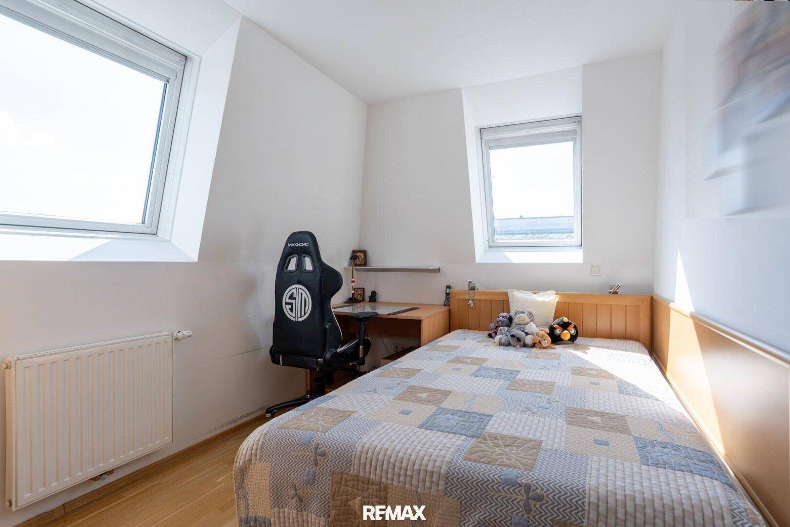 Helles Schlafzimmer mit Holzboden, Dachfenstern und einem Einzelbett mit Schreibtisch.