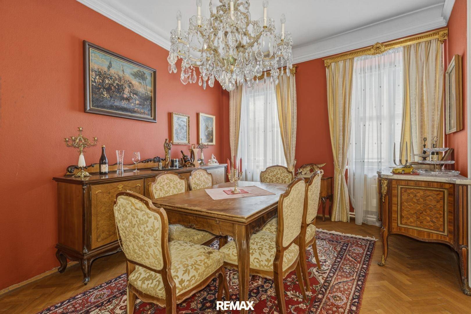 Klassisches Esszimmer mit roter Wandfarbe, elegantem Kronleuchter und antiken Holzmöbeln.