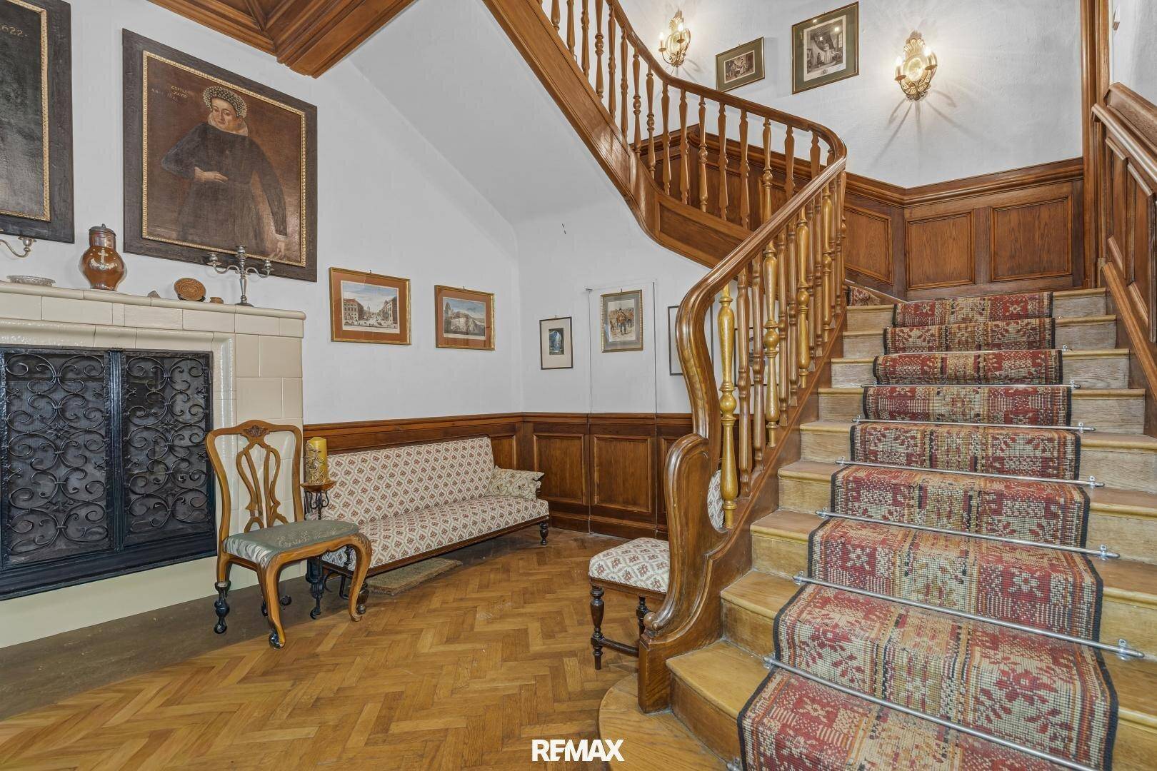 Elegantes Treppenhaus mit Holzvertäfelung, Teppichläufer und einem traditionellen Kamin.