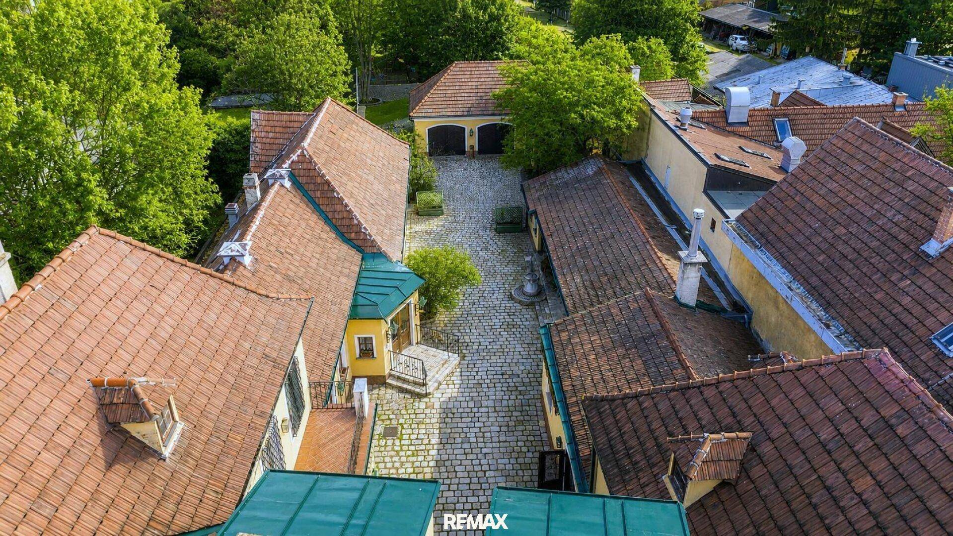 Luftaufnahme des Anwesens mit mehreren Gebäuden, Innenhof und umgebenden Bäumen.