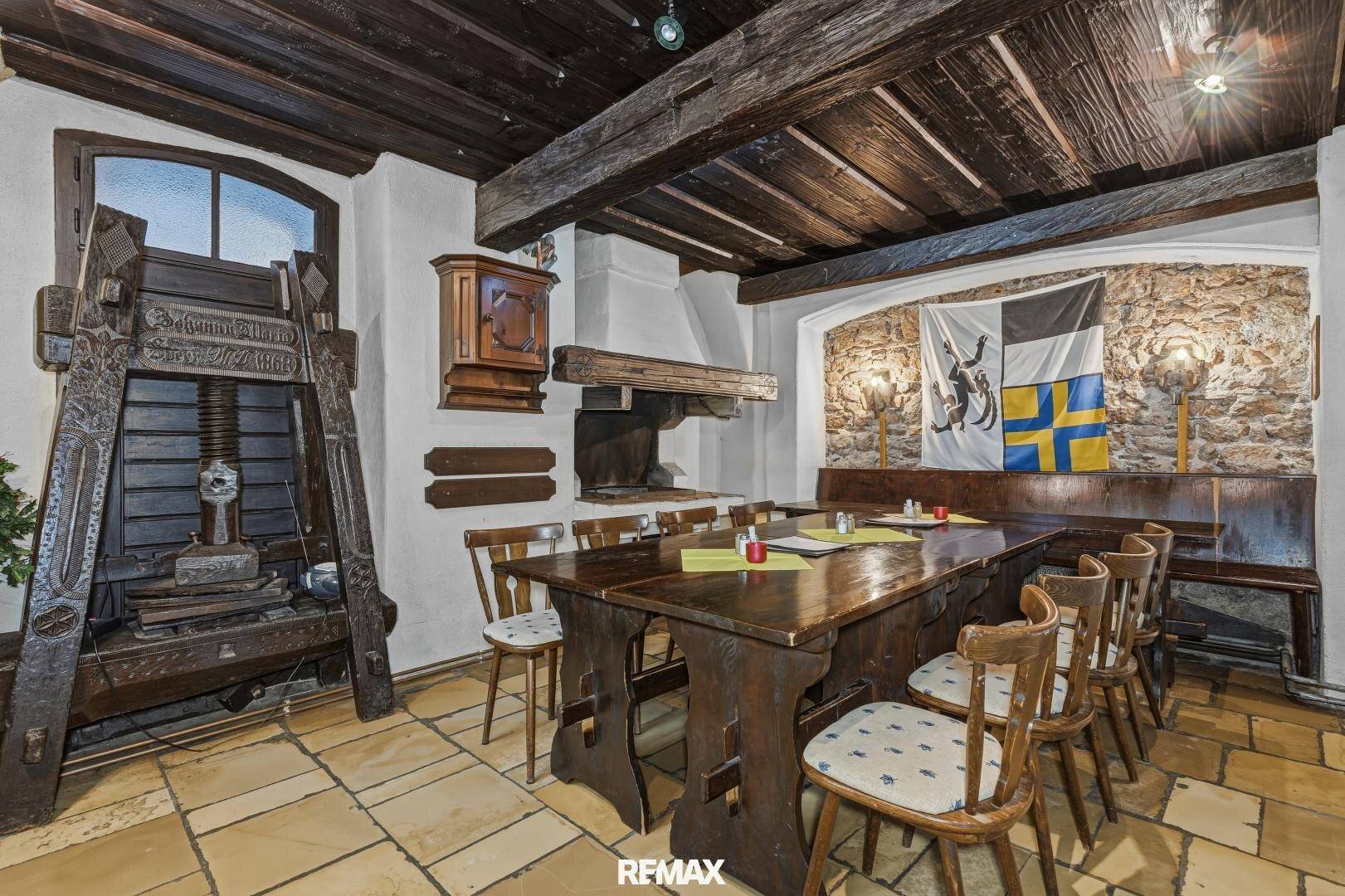 Traditioneller Speiseraum mit Holzbalkendecke, Steinboden und einem historischen Weinkelter.