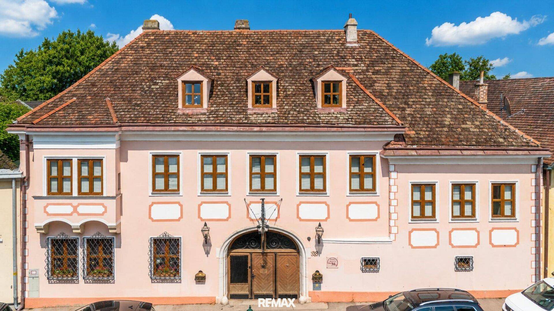Historische Fassade des Hauptgebäudes mit rosa Putz, braunen Fenstern und einem Ziegeldach.