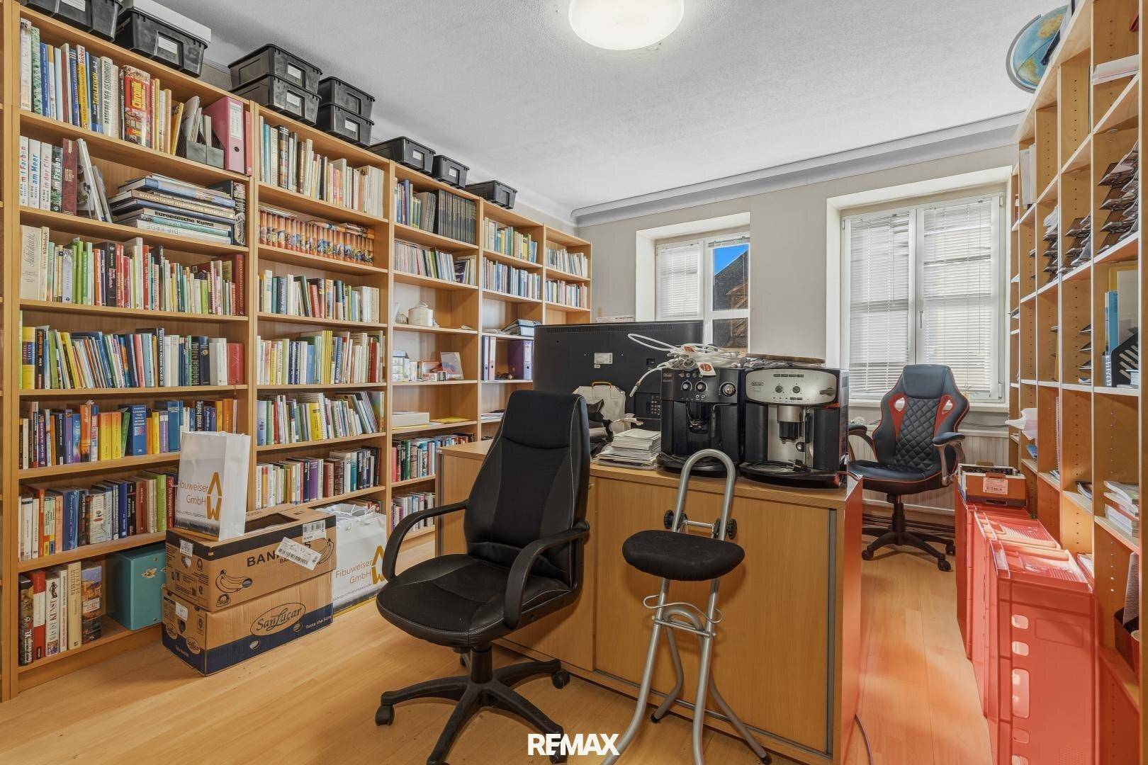 Arbeitszimmer mit raumhohen Bücherregalen, Holzboden und natürlichem Lichteinfall durch die Fenster.